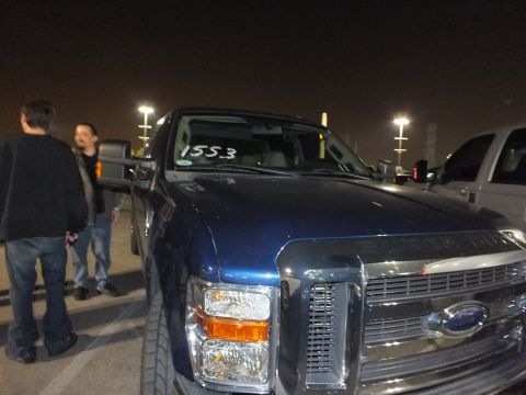 2003 Ford Crown Victoria - Blue Ford Super Duty truck front, 1553 marked on the windshield, two people standing alongside