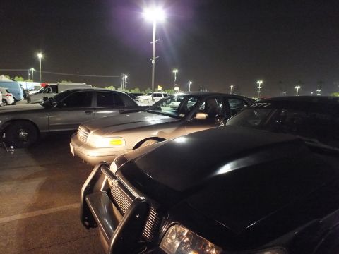 2003 Ford Crown Victoria - Tan Crown Victoria beside a black one in a floodlit lot, more vehicles fading into the dark