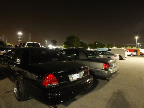 2003 Ford Crown Victoria - Black Crown Victoria with red tail lights beside a gray one, event tents in the distant lot