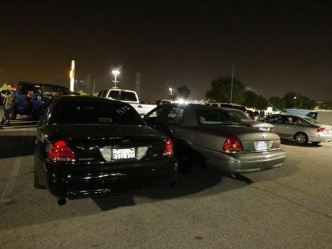 2003 Ford Crown Victoria - Black Crown Victoria rear wearing plate FYTLVTC next to a gray sedan in a busy night lot