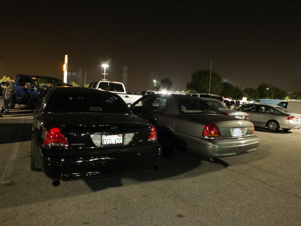 Black Crown Victoria with FYTLVTC plate and gray sedan parked at night meet