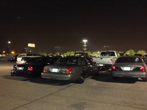 2003 Ford Crown Victoria - Several Crown Victoria sedans angled across a night lot, tail lights glowing under a light pole