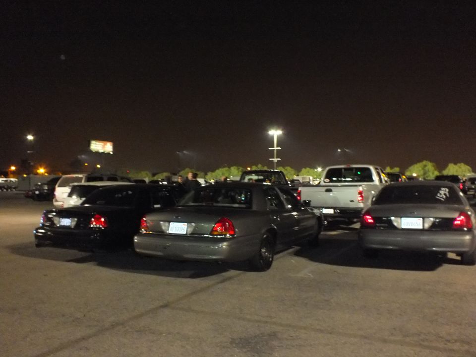 Black, gray and silver Crown Victoria sedans parked at angles in a dark lot