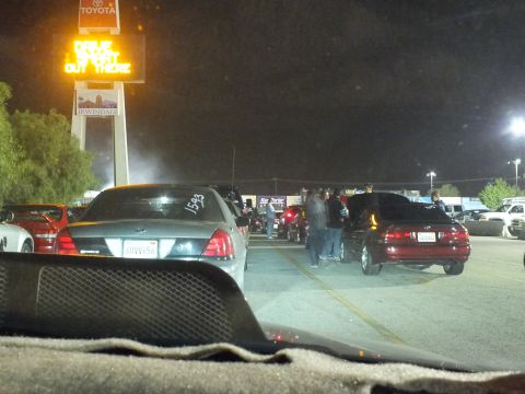 2003 Ford Crown Victoria - Gray Crown Victoria parked before the Toyota-topped Irwindale sign, crowd milling on the lane