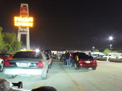 2003 Ford Crown Victoria - Vehicle lineup beside the illuminated Irwindale Speedway pylon sign, spectators gathered in the lane