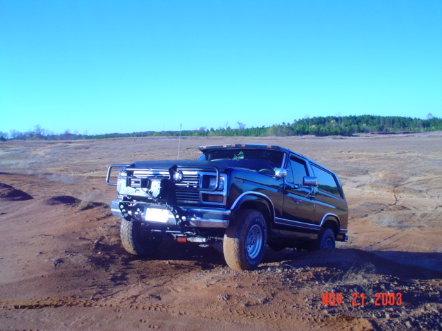 Black Ford Bronco with aftermarket bumper and lights on a dirt hill