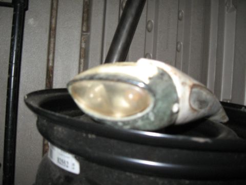 1994 Ford Bronco - Headlight assembly with a clear lens and white housing sits on a black rim.
