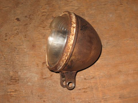 1994 Ford Bronco - A single, weathered headlight with a ribbed glass lens sits on a wooden surface.
