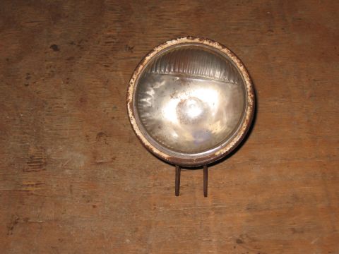1994 Ford Bronco - A single, vintage headlight with a rusty bezel and ribbed glass lens sits on a wooden surface.