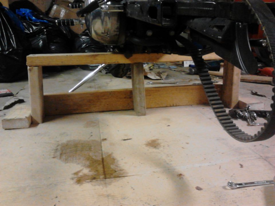 Motorcycle engine and drive belt supported by a wooden stand in a garage