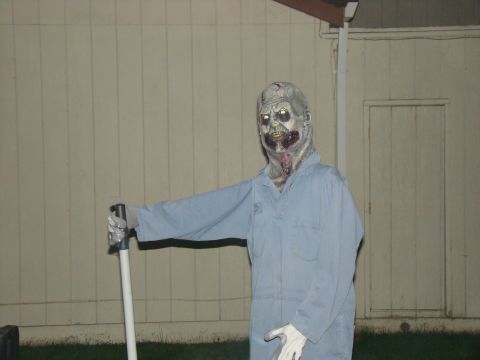 1989 Ford Bronco - A zombie decoration stands outside a building, dressed in light blue overalls and holding a pole.