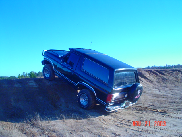 Black SUV climbing a dirt hill, spare tire on back. Photo dated 2003