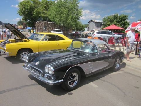 1991 Ford LTD Crown Victoria - A classic black Chevrolet Corvette is displayed at an outdoor car show next to a yellow muscle car.