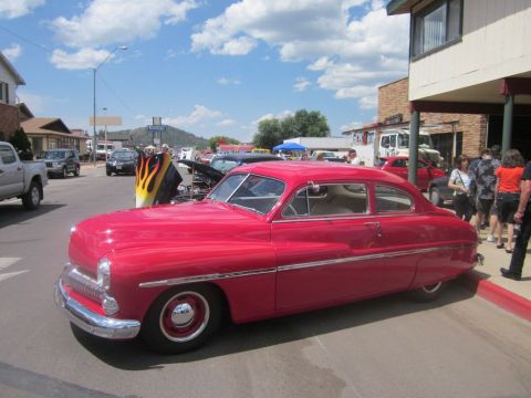 1991 Ford LTD Crown Victoria - A red 1950s sedan with flame decals on the hood is displayed at an outdoor car show.