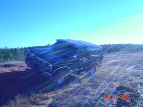 1986 Ford Bronco - This 1986 Ford Bronco is captured in a three-quarter front view while navigating a sandy, off-road terrain under a clear blue sky.