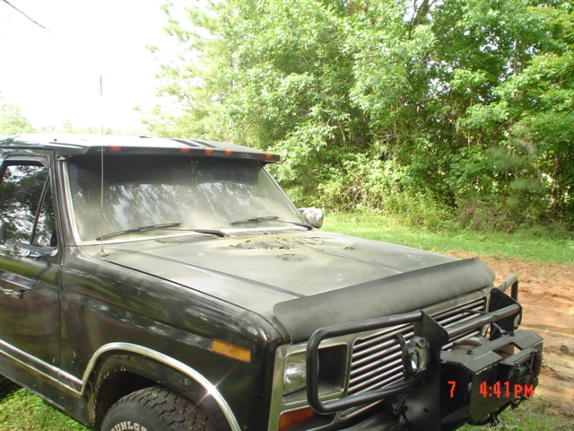 Front end of a dark-colored Ford Bronco with a bug deflector and brush guard. The hood has several dents