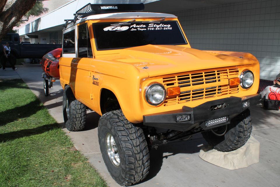 Orange Ford Bronco with Yakima rack and custom bumper. Has 'Bronco' badge on fender and 'RAD Auto Styling' sticker on windshield