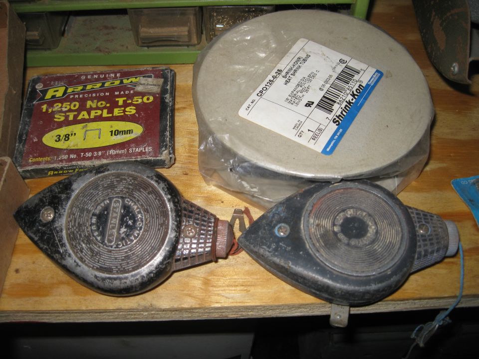 Two chalk line tools and a box of Arrow staples on a wooden shelf