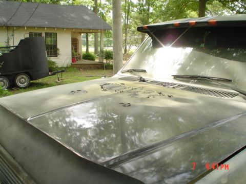 1986 Ford Bronco - The hood of a vehicle shows significant wear and tear, with peeling paint and rust evident.
