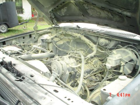 1986 Ford Bronco - The engine bay of a dusty vehicle is shown with the hood open, revealing the engine components.
