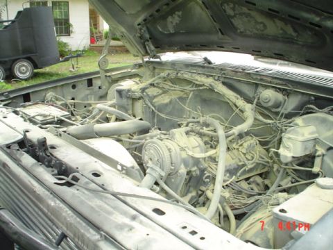 1986 Ford Bronco - Engine bay of an older truck, covered in dust. The hood is open, revealing the engine and various components.
