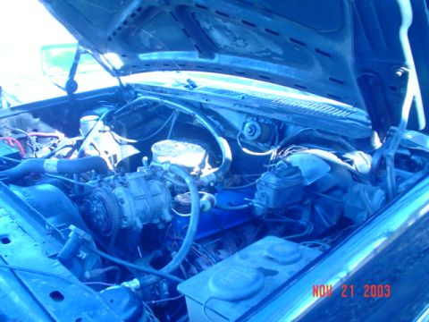 1986 Ford Bronco - The engine bay of a vehicle shows signs of water damage and wear, with various components visible under the open hood.