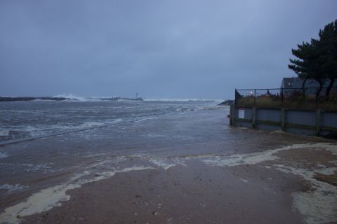 1990 Ford Bronco - A flooded beach and roadway with rough waves crashing ashore, likely during a storm event.