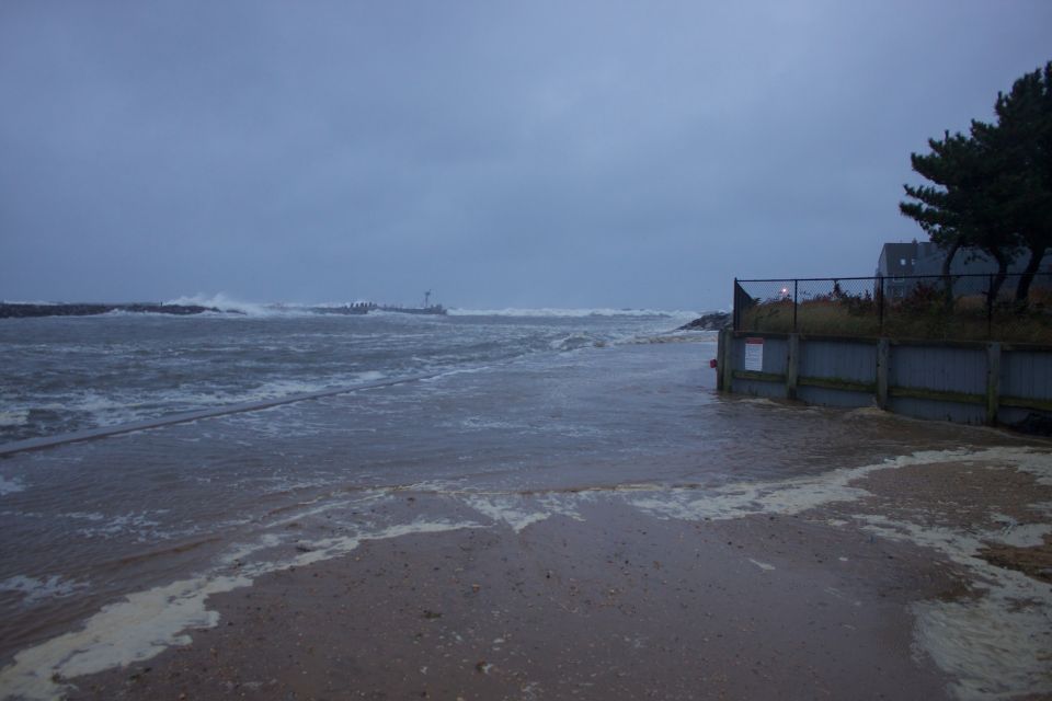 Flooded beach with rough waves and a fence, during a storm