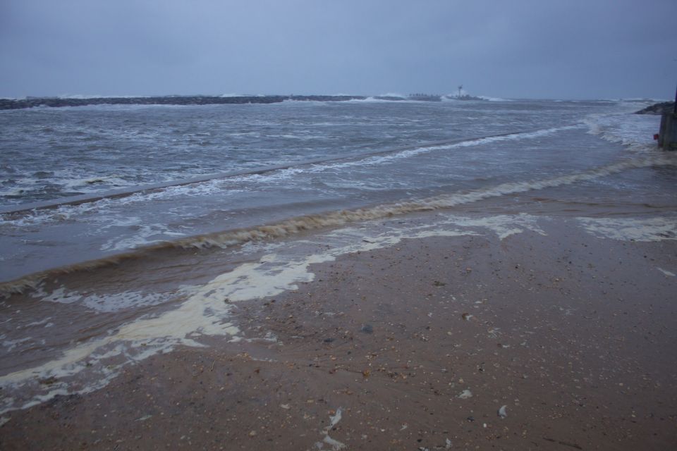 Beach with foamy waves and a distant breakwater under a cloudy sky