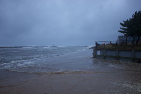 1990 Ford Bronco - A turbulent ocean scene during a storm, with waves impacting a jetty and inundating a sandy area.
