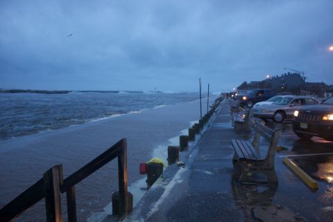 1990 Ford Bronco - Vehicles are parked along a wet boardwalk as waves crash onto the shore during a storm.