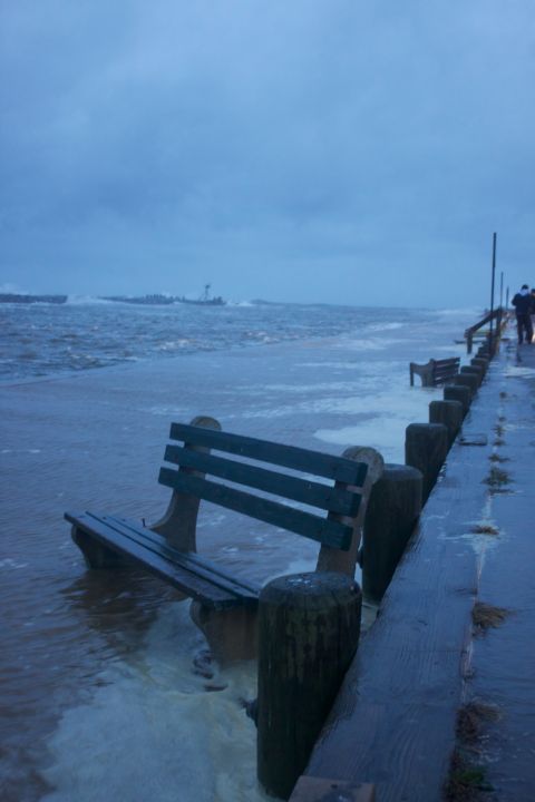 1990 Ford Bronco - A bench sits on a flooded boardwalk as waves crash ashore under a gloomy sky.