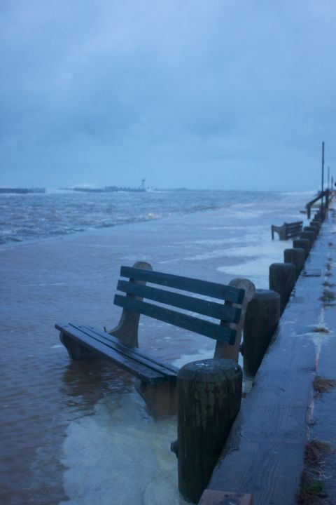 1990 Ford Bronco - A park bench is submerged in floodwaters next to a pier, with waves crashing and a distant lighthouse visible.