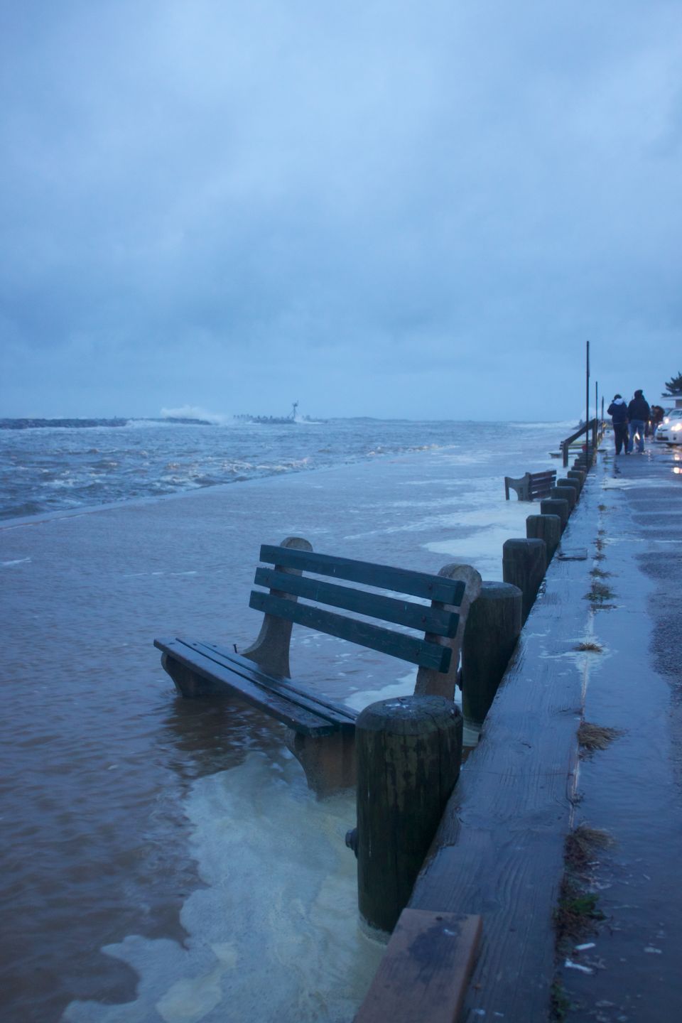 Flooded boardwalk with benches and people walking during a storm