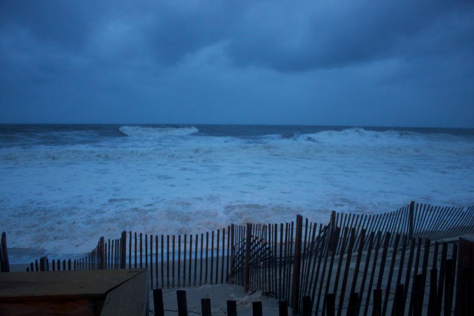 Stormy ocean with large waves crashing, viewed from a beach with a wooden fence