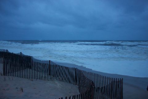 1990 Ford Bronco - A desolate beach scene with a wooden fence and rough waves under a dark, cloudy sky.