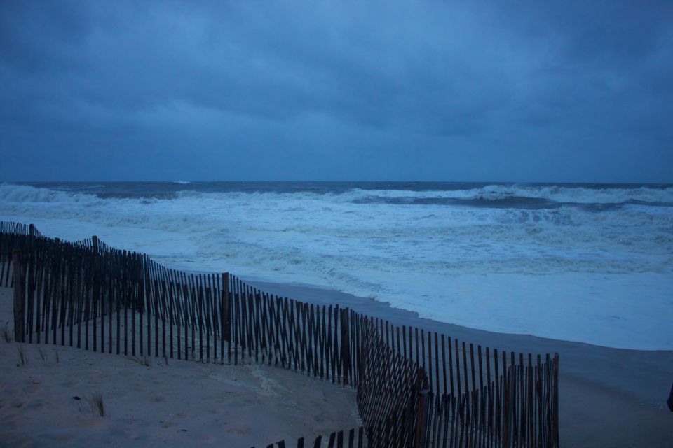 Beach scene with dark stormy clouds, rough ocean waves, and a wooden sand fence in the foreground