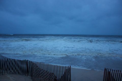 1990 Ford Bronco - Ocean waves during a storm, with a wooden fence in the foreground. Supermotors.net logo present.