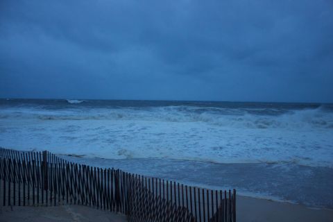 1990 Ford Bronco - The ocean churns under a dark, cloudy sky, with waves breaking near a sandy beach and fence.