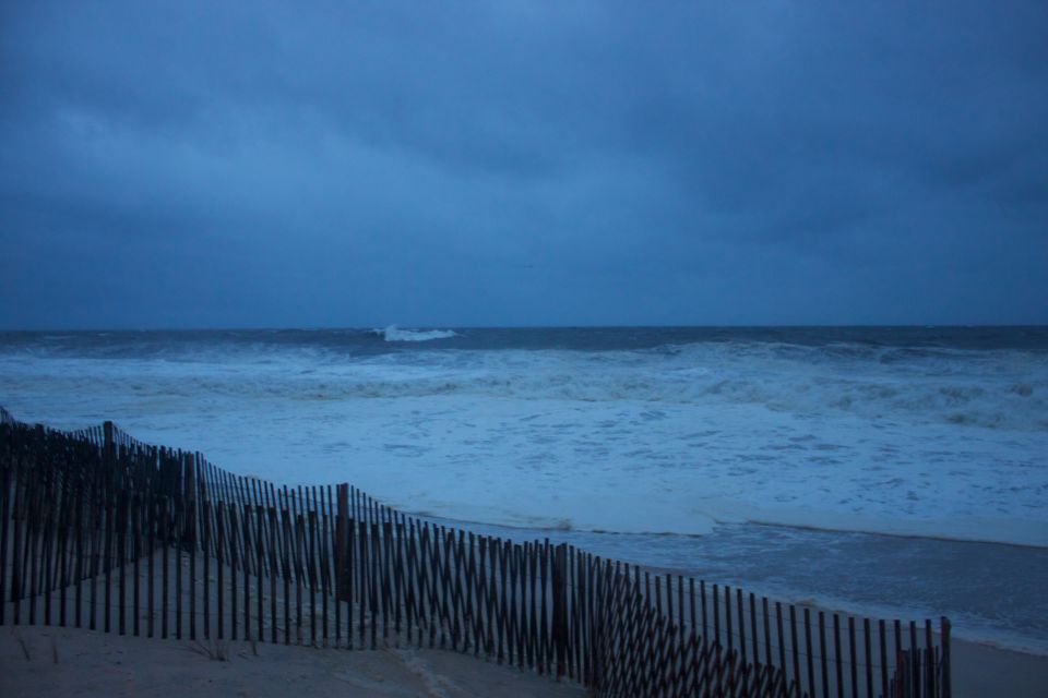 Beach fence with choppy ocean waves under a dark, cloudy sky