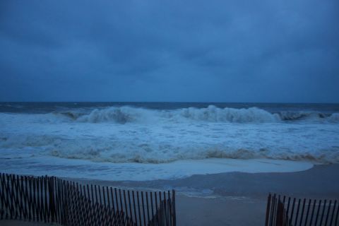 1990 Ford Bronco - Rough seas and choppy waves batter the shore under a cloudy sky, with a fence marking the edge of the beach.