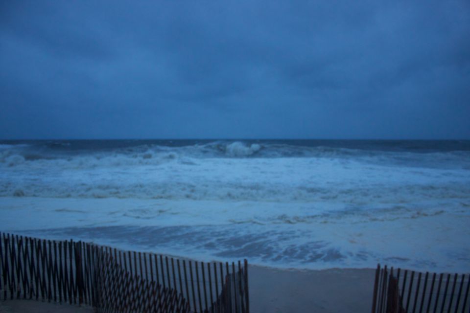 Stormy ocean waves crash on the beach behind a wooden fence