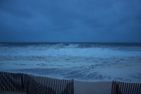 1990 Ford Bronco - Ocean waves during a storm, with a wooden fence in the foreground. Supermotors.net logo present.