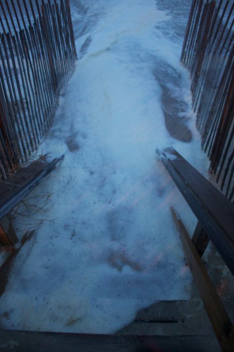 1990 Ford Bronco - Foamy ocean water washes over a wooden walkway and stairs, with fences lining the path.