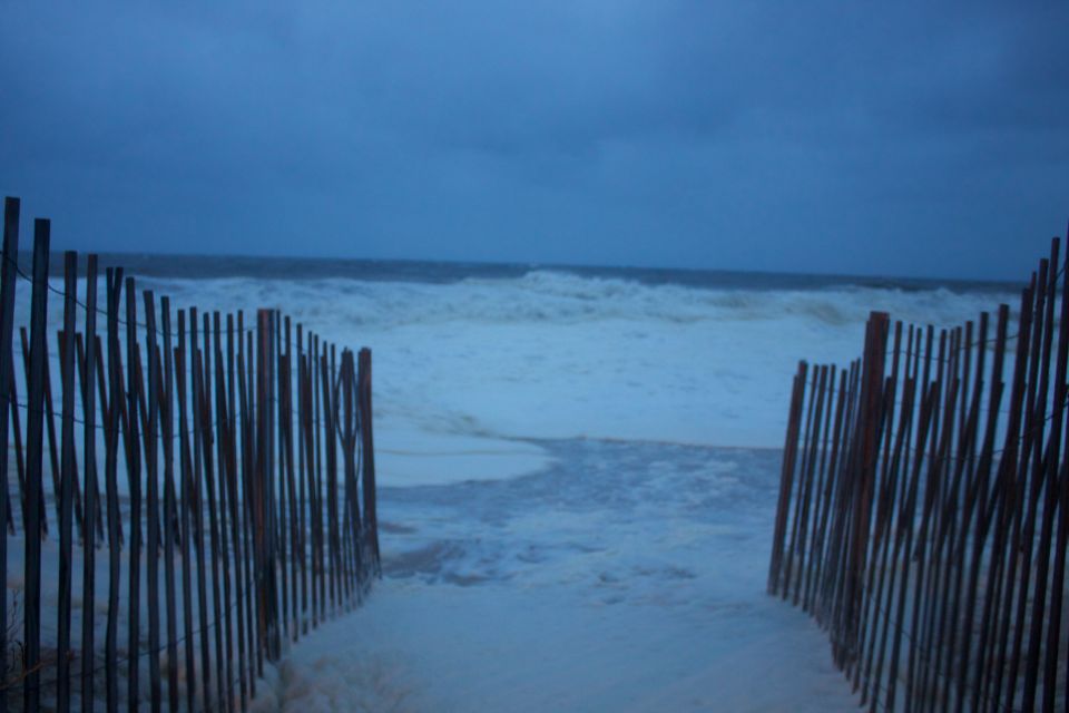 Wooden fence on a beach with foamy waves and dark sky