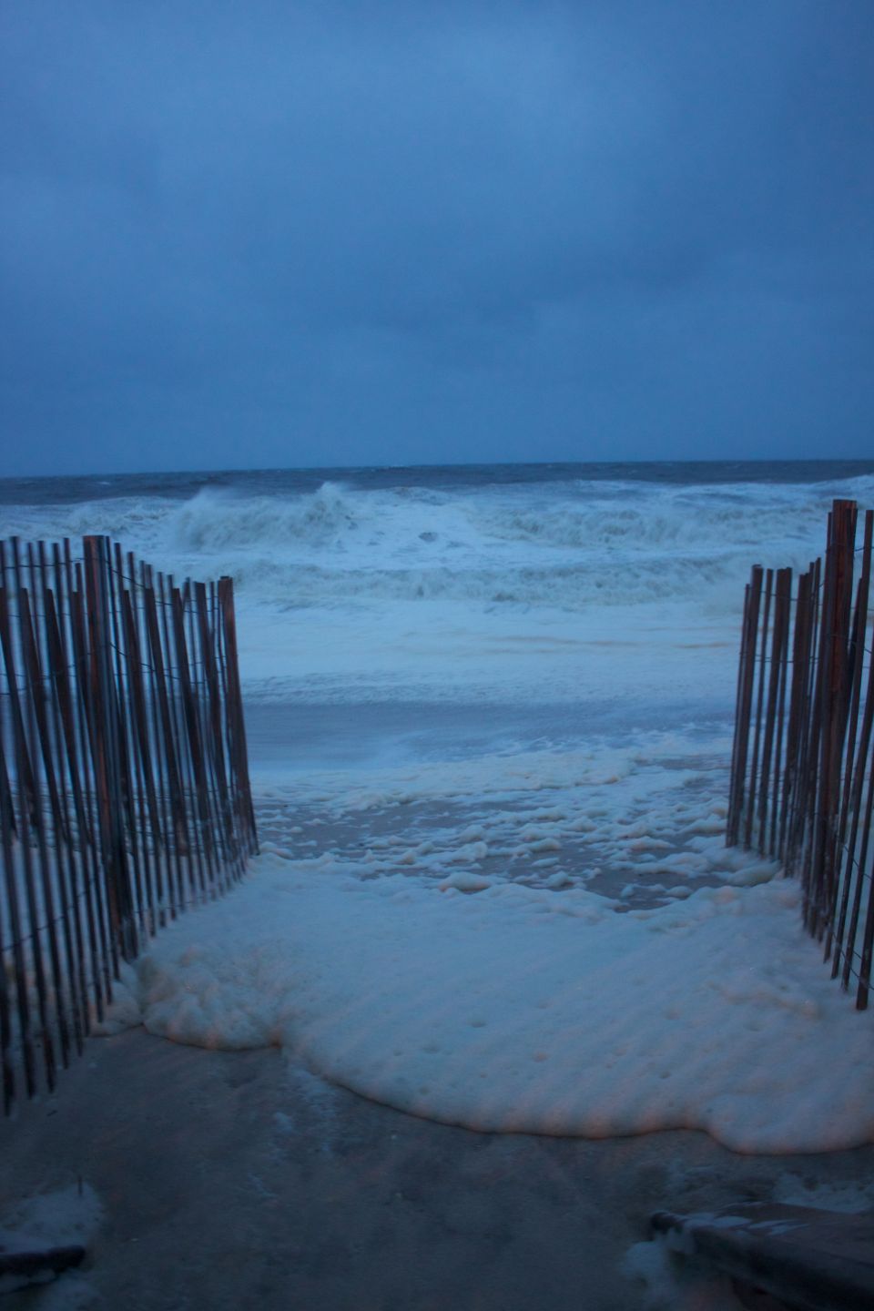 Stormy beach with rough waves, sea foam, and a wooden fence