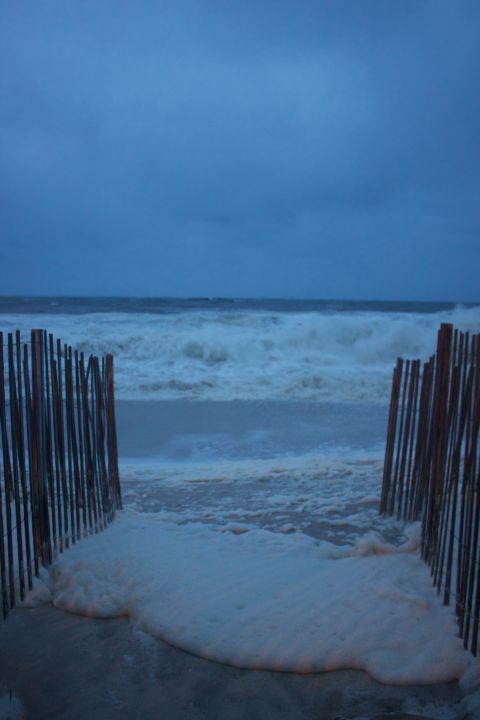 1990 Ford Bronco - A stormy beach scene with foamy waves crashing ashore, framed by wooden fence posts. The Supermotors.net logo is visible at the bottom.
