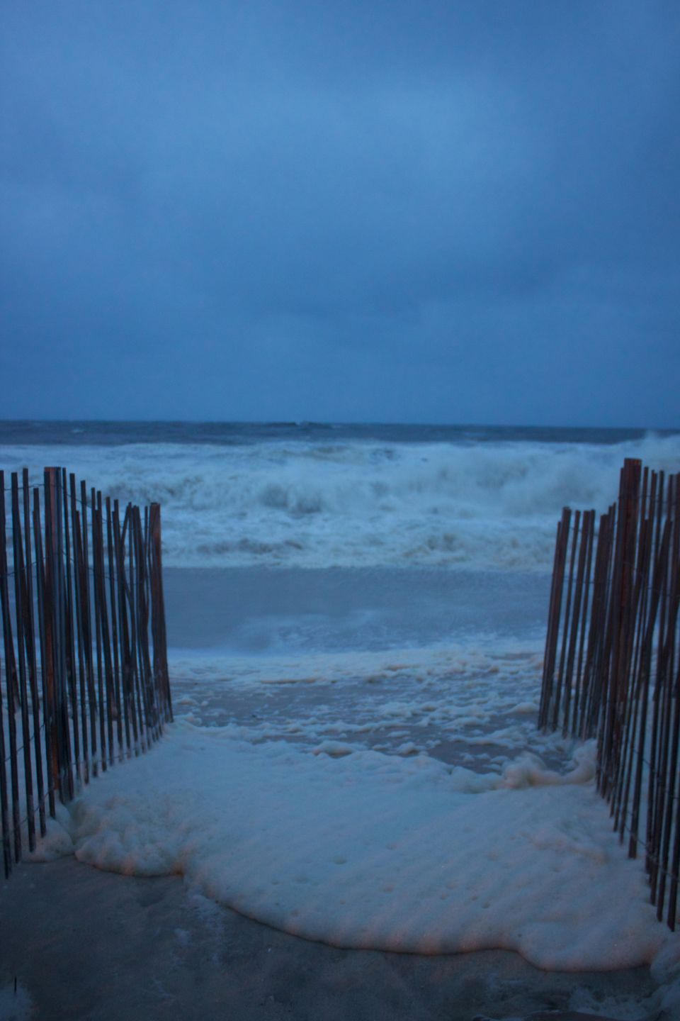 Beach scene with rough waves and foam, wooden fence posts, and Supermotors.net watermark