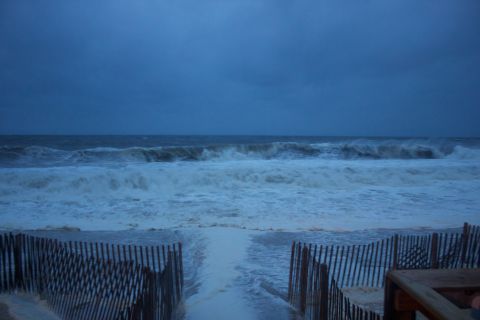 1990 Ford Bronco - Large waves roll in under a dark, cloudy sky, with a wooden fence line bordering the beach.