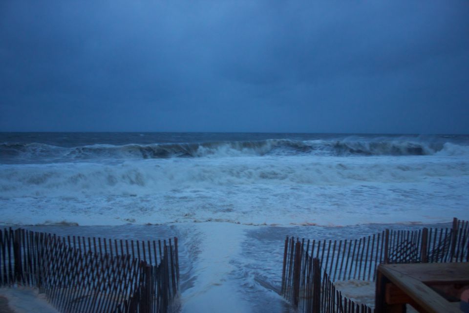 Stormy ocean waves crash on the beach with wooden fences in the foreground